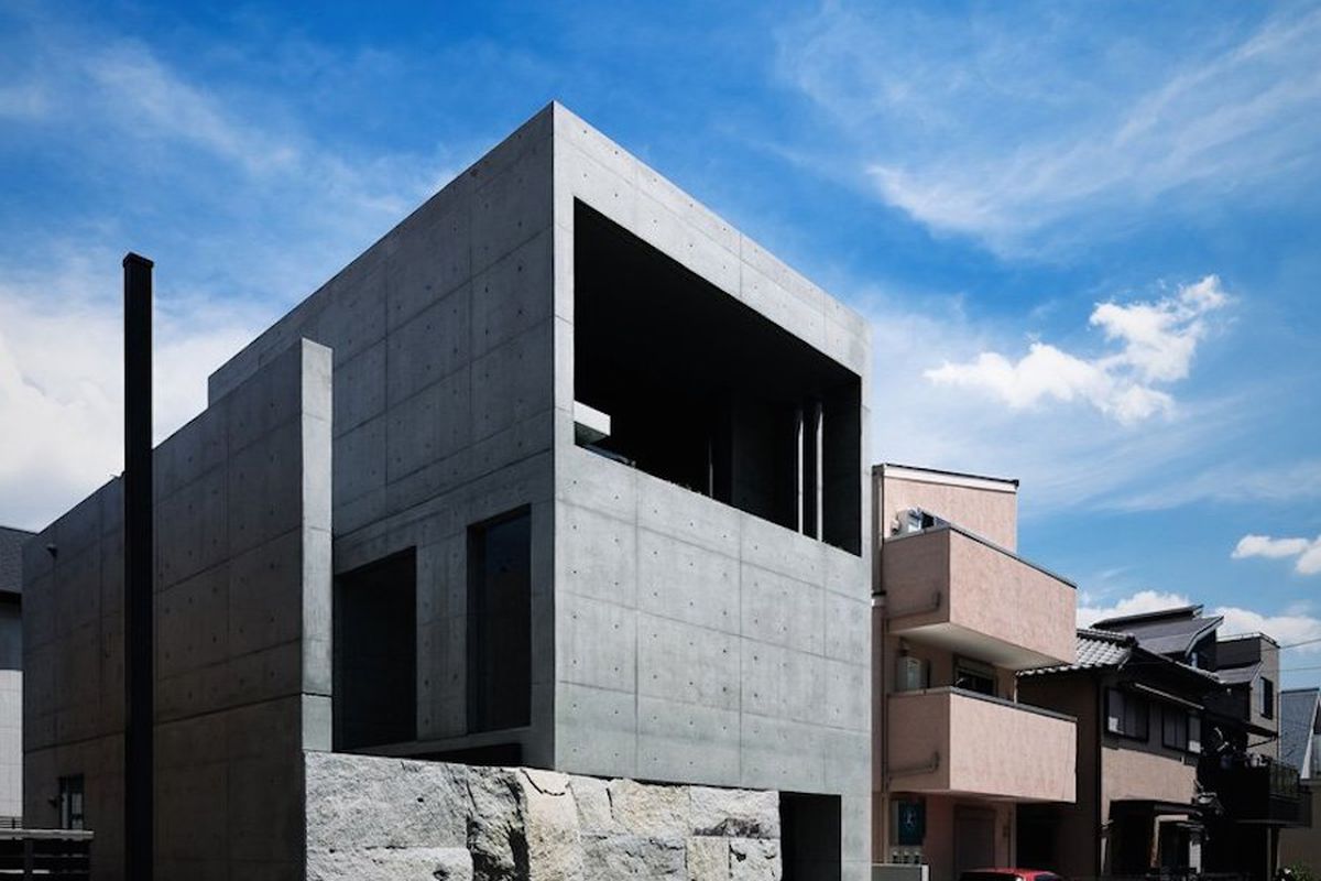 Boxy concrete house rests on stone base. 